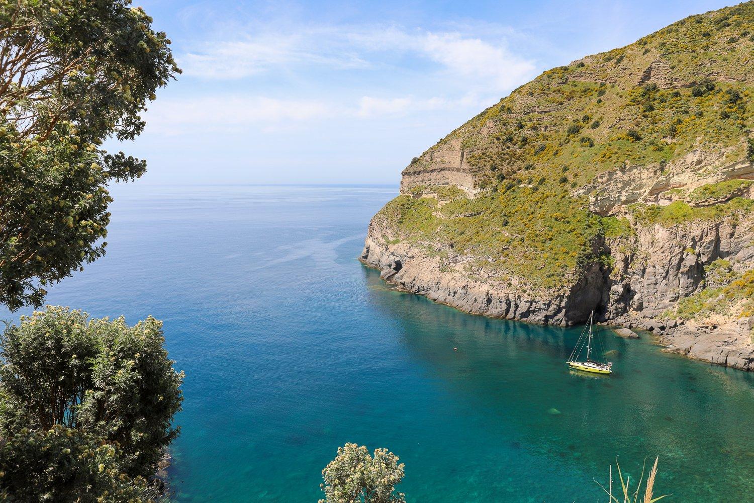 Sailboat roaming around the waters of Baia di Sorgeto. In this guide to Ischia, Italy, you