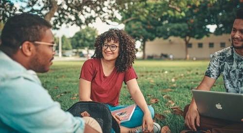 Three students sat talking in an outside green space